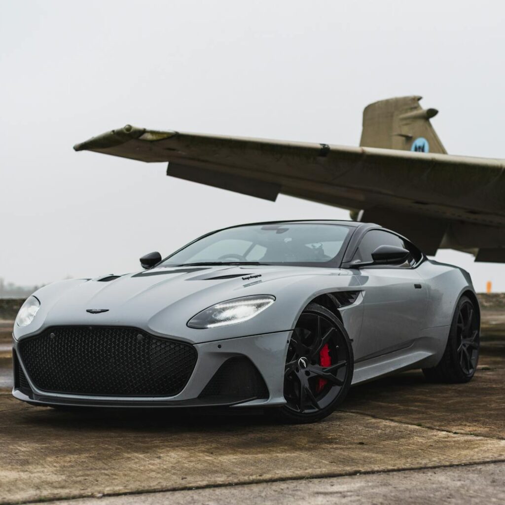 Photo by Bob Ward Sleek grey luxury car parked beneath an old aircraft on a foggy day.