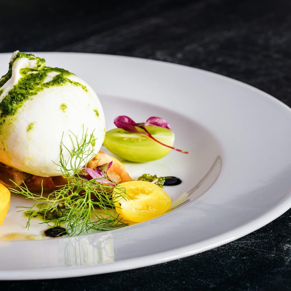 Delicious burrata salad with fresh heirloom tomatoes and pesto, plated elegantly.