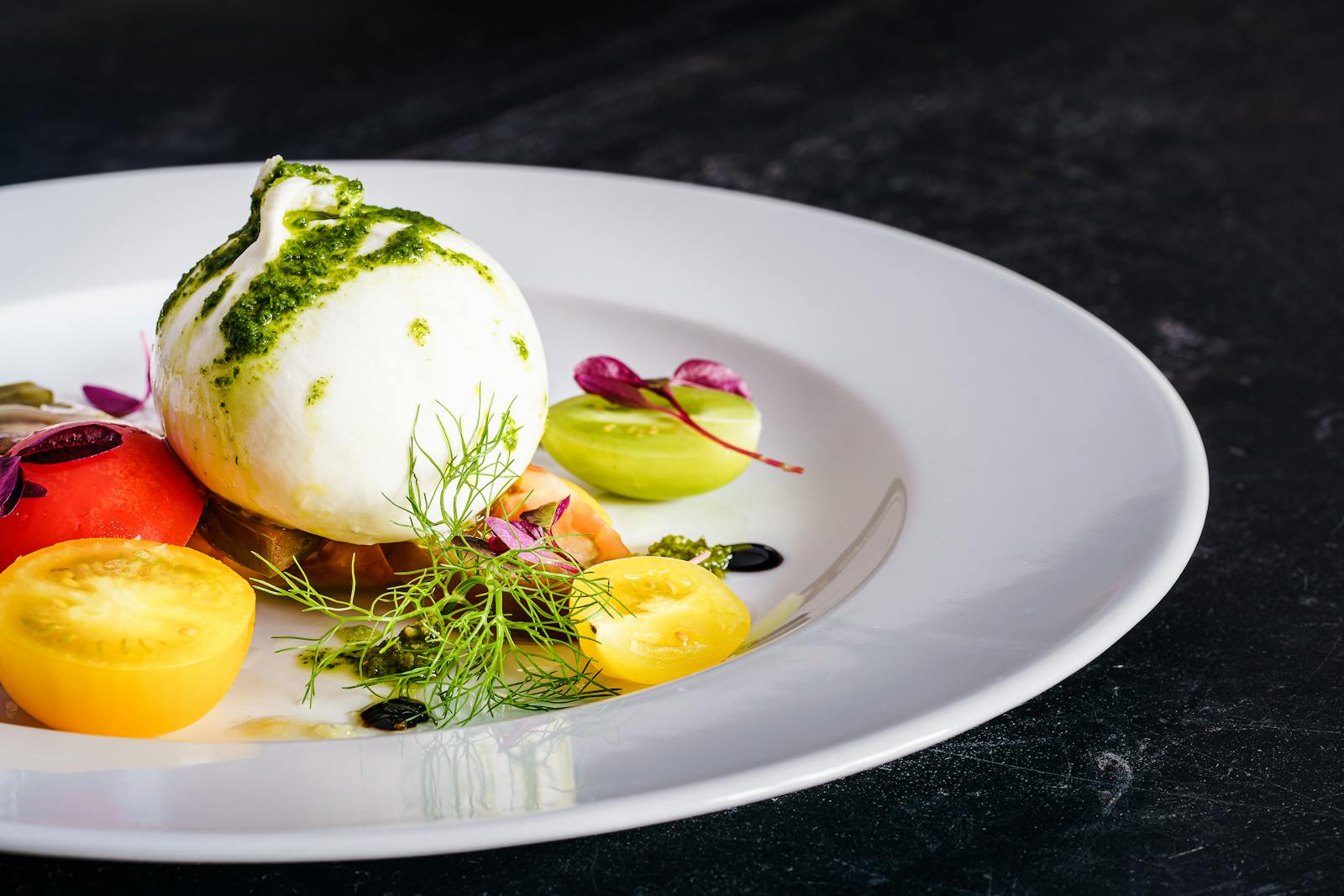 Delicious burrata salad with fresh heirloom tomatoes and pesto, plated elegantly.