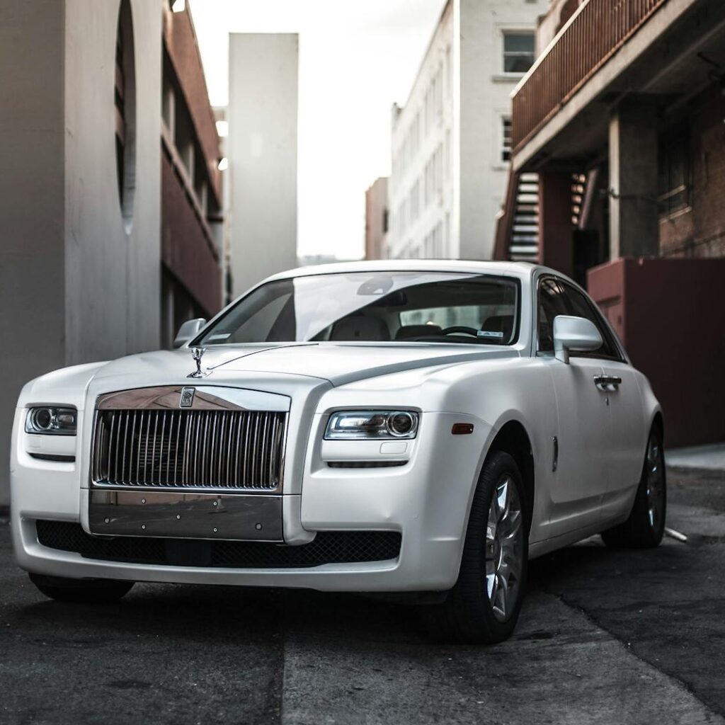 Photo by jae p Elegant white luxury car parked in an urban alley, exuding sophistication and style.