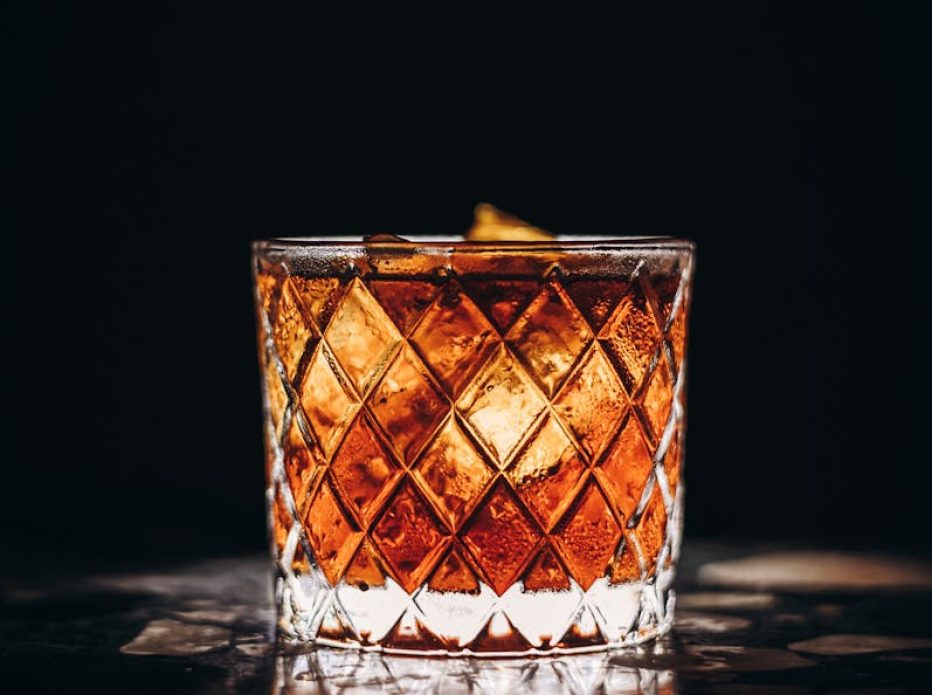 Close-up of a whiskey glass with ice reflecting on a dark surface.
