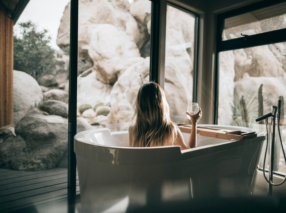 woman in white bathtub holding clear drinking glass